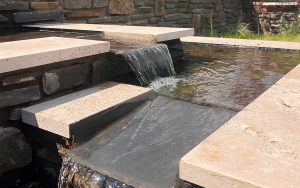 Stone and slab water feature with stonework wall cascading down a landscaped wall - designed and built by Evergreen Wales in Llandaff
