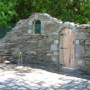 Stonework archway with windows and timber door with stonework ground and water feature - designed by Evergreen Wales