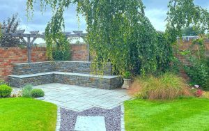 Stone wall with seating and new patio with shingle pathway to house and new lawn. Designed and built by Evergreen Wales for a property in Penarth.