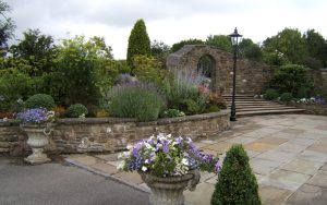 Stonework garden and archway with a hand built wall with metal ornate gate with flowers and stem design. Designed and built by Evergreen Wales.