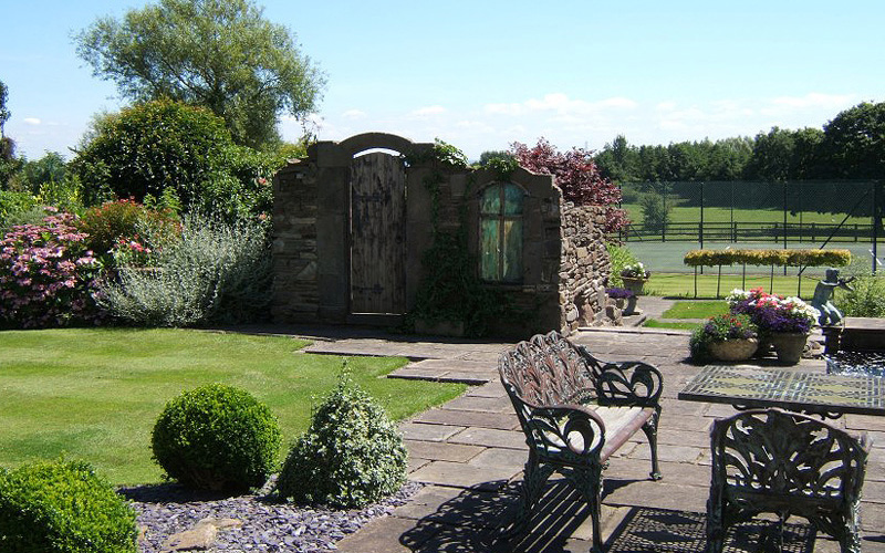 Stonework garden folly with door archway and obscured window in garden design. Designed and built by Evergreen Wales.