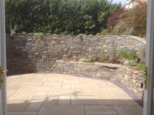 Stonework wall designed and installed by Evergreen Wales with shingle border and soft landscaped plants.